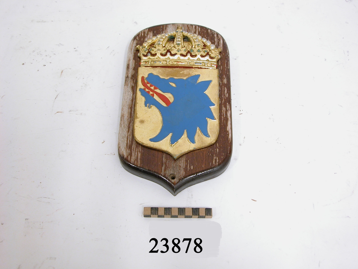 Vapensköld gjuten av mässing, krönt med kunglig krona, målad i heraldiska färger (färgerna skavda samt ärgbelagda). Botten i guld, därpå ett avslitet blått varghuvud med röd tunga och röda tänder. Skölden är fästad vid fernissad platta av trä. Symboltolkning: "Vidar- som var son till Oden- dräpte underjordens odjur Fenrisulven, vars huvud utgör vapensymbol". Källa: Stadsheraldiker Jan von Konow.