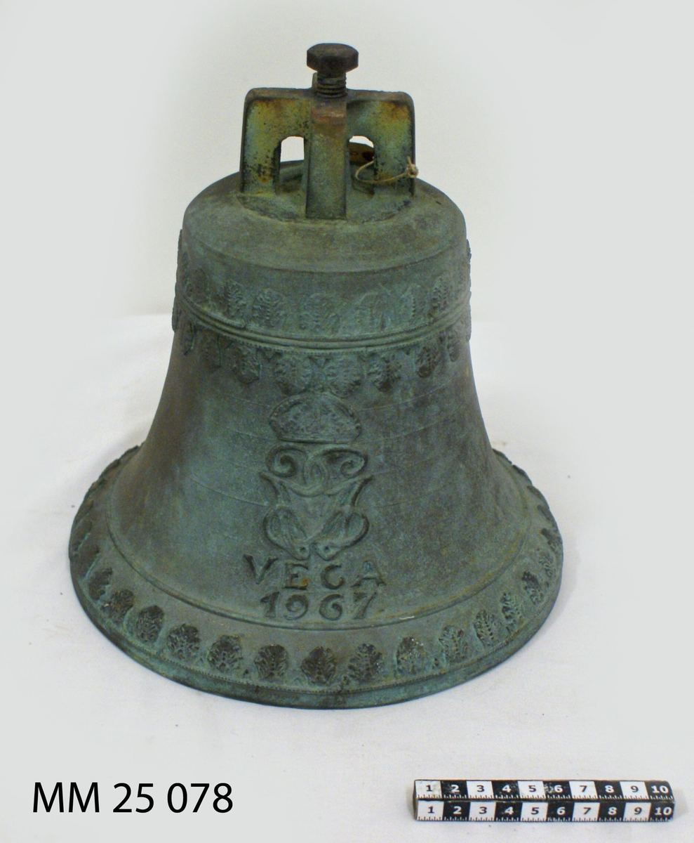 Skeppsklocka av brons märkt i relief: "Vega 1967" samt Gustaf VI:s monogram. Ornamentslinga i relief längs klockans topp och mynning. Kläpp saknas.