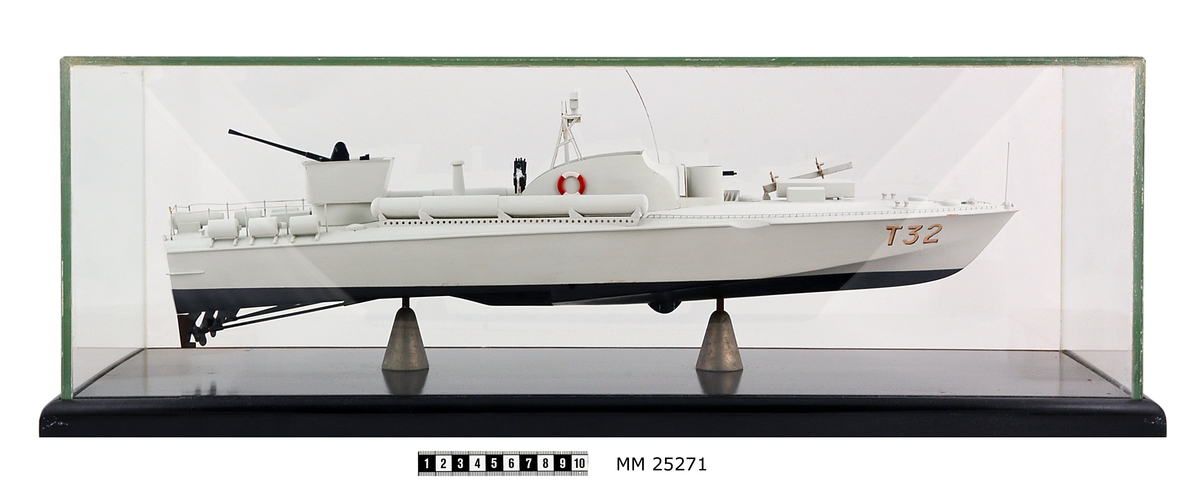 Modell av motortorpedbåten T 32. Från vattenlinjen och neråt målad i svart, från vattenlinjen och uppåt målad i ljusgrått. Märkt på stäven med skuggade bokstäver i guldfärg: "T32". På fördäck står en lysraketkastare och i en upphöjd brunnskonstruktion en dubbel KSP M/36. Mitt på fartyget en brygga med styrratt. På var sida om och bryggans sköldliknande upphöjning sitter en röd och vit frälsarkrans och något akter om dessa dubbellavettage med kulspruta M/36. Akter om bryggan sitter en luftvärnskanon i ett upphöjt brunnslavettage.
Modellen sitter på två konliknande fästen i en glasmonter med svart botten. Dimensioner avser modellen.