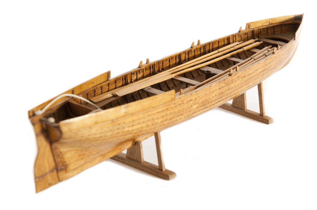 Gigg, bordlagd på spant, klink med fullständig inredning. 6 årtullar, 6 åror. Roder med skädda. Fernissad, Stativ fernissat. Masten saknas.