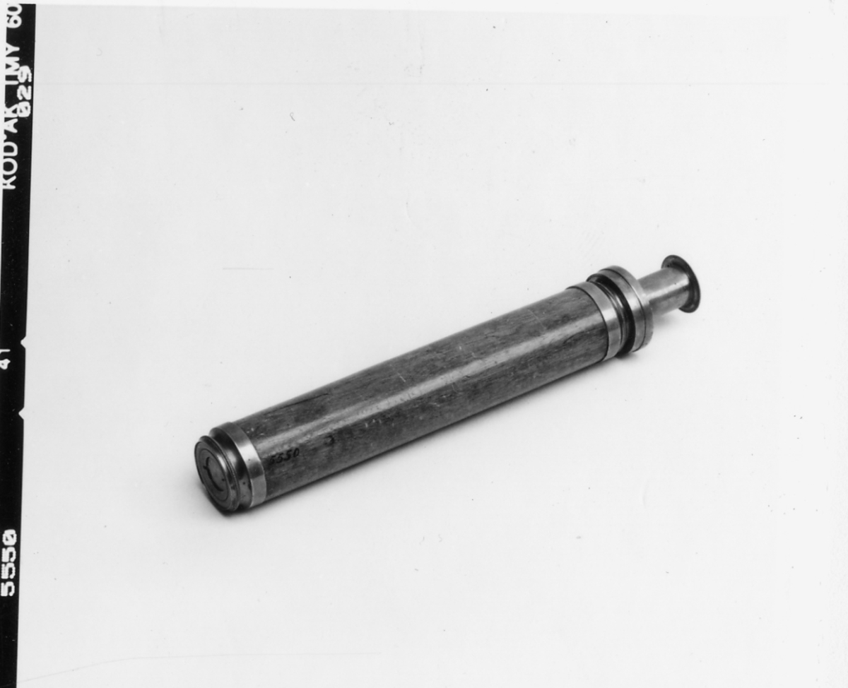 Tub av fernissad mahogny med insatstuber av mässing. Okularet försett med distansskala i alnar.