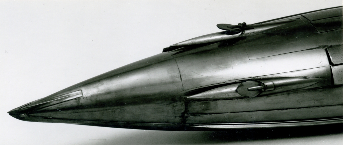 Spolformad. Stålplåt. Slingerköl, 2 propellrar av metall, 2 st höjd- och sidoroder parallellkopplade med gardjärn. 2 st höj- och sänkbara periskop av mässing. 4 st rännor för torpeder, därav 2 med luckor framtill, dels 2 för magasinering. Kort cylinder, rörlig i ränna midskepps akterut. Torpedrännorna täckas av långa stållock. Tillhörande 4 st torpeder av massiv mässing. Eneroths förslag till ubåt 1897. UndervattenstorpedFöremålets form: Spolformad.