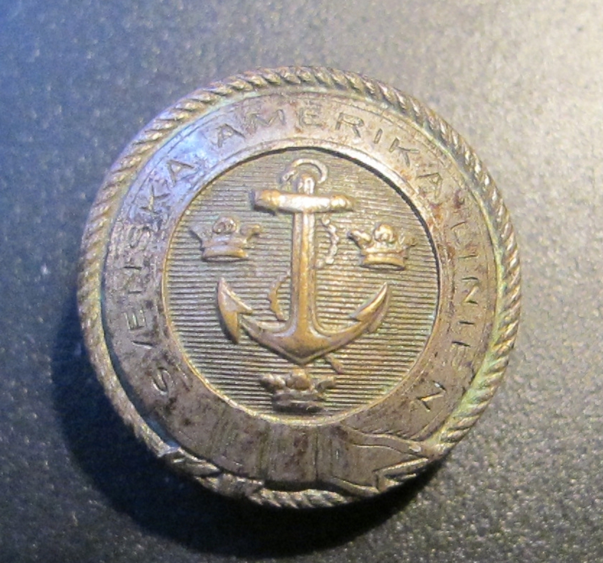 Runda, konvexa, metallknappar med präglat ankare omgivet av SAL:s emblem med tre kronor mot räfflad bakgrund, inramat av en slät bård i form av ett band med texten SVENSKA AMERIKA LINIEN, avslutas mot kanten av en repdekor.

Baksidan pålödd ögla för fästande av knappen på plagg, två hål, texten: C.C. SPORRONG & CO STOCKHOLM.