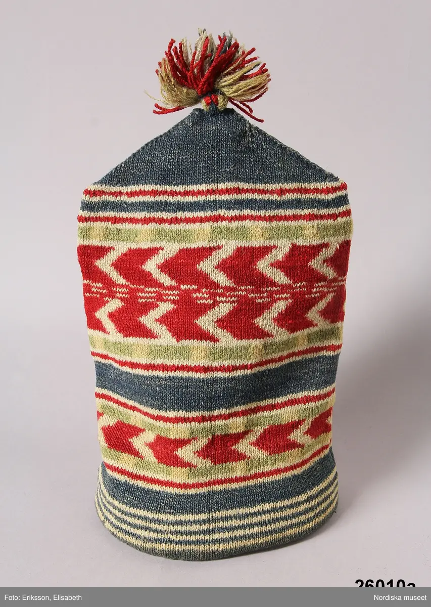 2 st röda toppluvor, A-B.
A.
B.Röd toppluva, maskinstickad i slätstickning av ullgarn, filtad, 2 stycken med nästan osynliga sidsömmar, hoptagningar i toppen. Liten röd ullgarnstofs högst upp. Nederkanten uppvikt 2 varv.

Berit Eldvik okt 2005