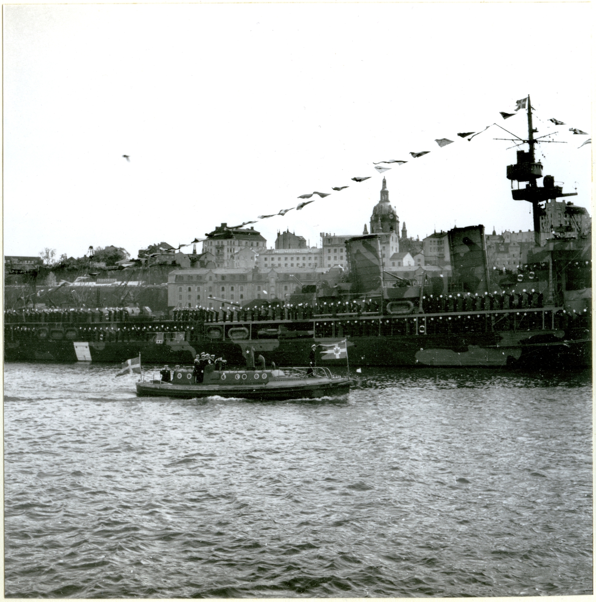 [från fotobeskrivningen:] [---] "Besättningen på HMS GOTLAND mannar reling hälsande HM Gustav V när denne passerar ombord i flaggskeppets motorbarkass. Foto taget på Stockholms ström i början av 1940-talet." [---]