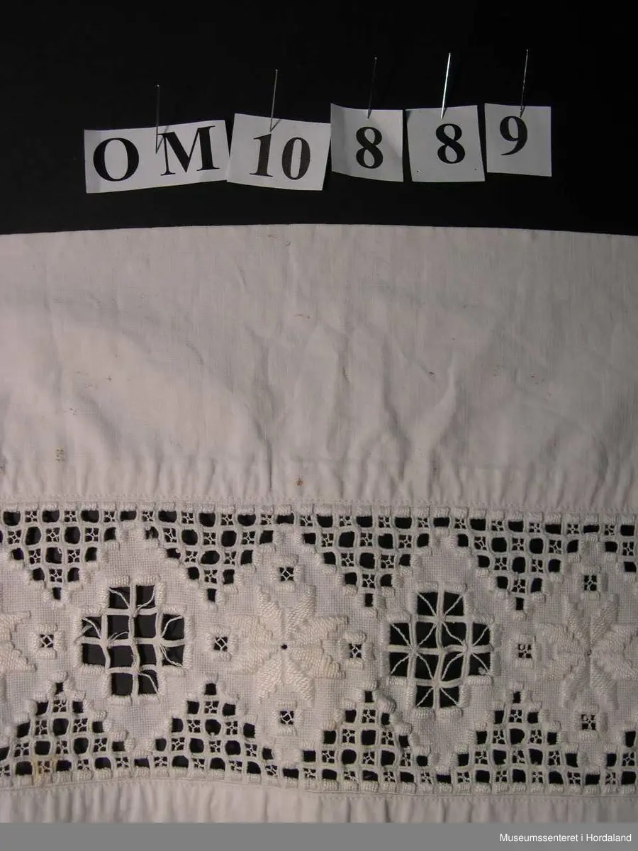 Form: bunadsforkle med linning og band i livet, knappa bak, innfeld broderi nedst på forkle
