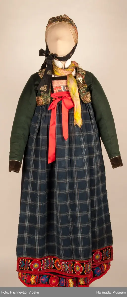 Kone fra Nedre Hallingdal i hallingbunad.  Kona står utstilt i den faste bunadutstillingen på Hallingdal Museum, Nesbyen.  Hallingbunaden består av mange draktdeler; trøya HFN 01835, Forkle HFN 03381, stakk, liv, lue, silketørkle rundt lua, silketørkle rundt halsen HFN 03500, bringduk og skjorte.