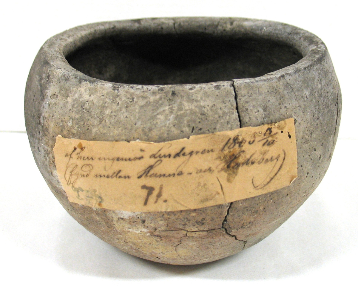 00 276. Enl. gammal lapp lösfynd 1865 vid järnvägsbygge vid Hästevadet V. Tunhems socken, Västergötland. Urnan hör således till det tidiga järnåldersgravfältet vid Hästevadet V. Tunhem.

Se vidare Svenssons rapport till R. Å. av den 17 oktober 1950. Se synnerhet sid. 8. (Enligt tryckta 
 katalogen nr 277). Köpt enligt gammal lapp: av herr Ing. Lindgren den 15. 10. 1865.
 

Lerurna, rundad. Kanten inåtböjd, oglasserad. Hål. Brända ben och kolblandad jord i urnan. 
 
Höjd. 6,2 cm.
 

Från Vänersborgs Läroverks samling. Till Vänersborgs museum 1886.