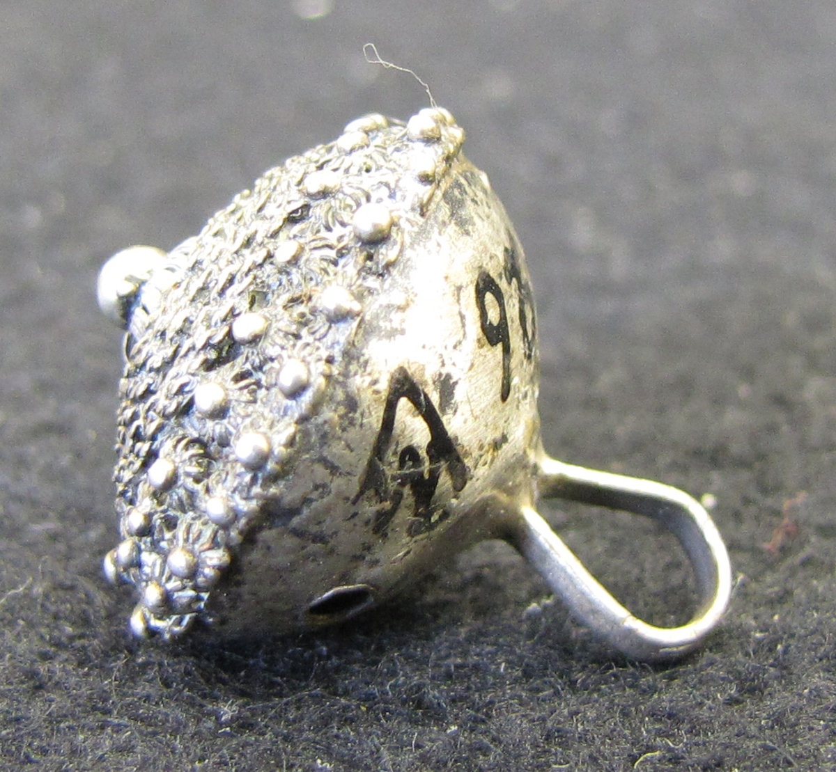 Silverknapp med riklig filigrandekor på ovansidan. Enligt museets katalog 1904-05 härrör knappen från Norge.