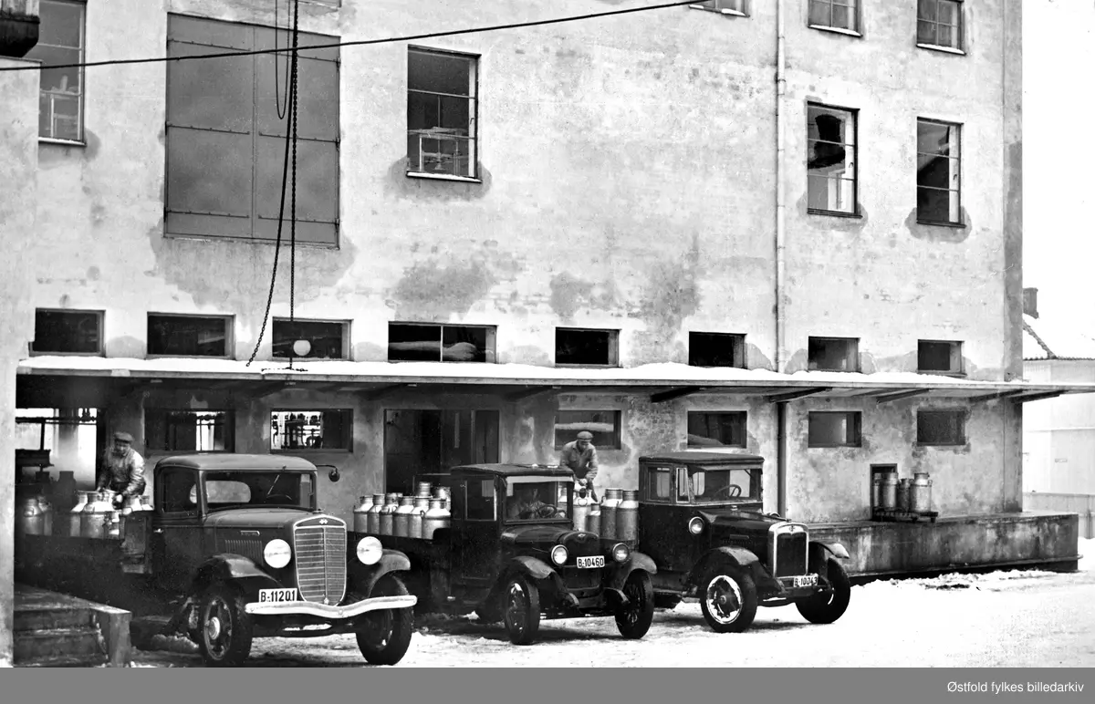 Fredrikstad Aktiemeieri 1938.
"Utekspedering". Lasterampe på meieriet. 3 lastebiler, 2 menn laster på melkespann på bilenen. 1 sjåfør. 

Bilene er en International  B-11201  Chevrolet B-10460  og International B-11043.