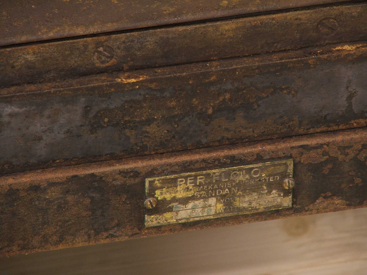 Flølo komfyren. Elektrisk komfyr. Med tank for varmt vatten (oppå bak), og kran for tapping av det varme vatnet framme. To kokeplater oppå. Fem runde brytarar framme i front. Ei uttrekkbar plate under. Omnsdør til å opne inn til steikjeomnen under der att. To plater med handtak inne i steikjeomnen. Komfyren står på fire bein (av jarn).