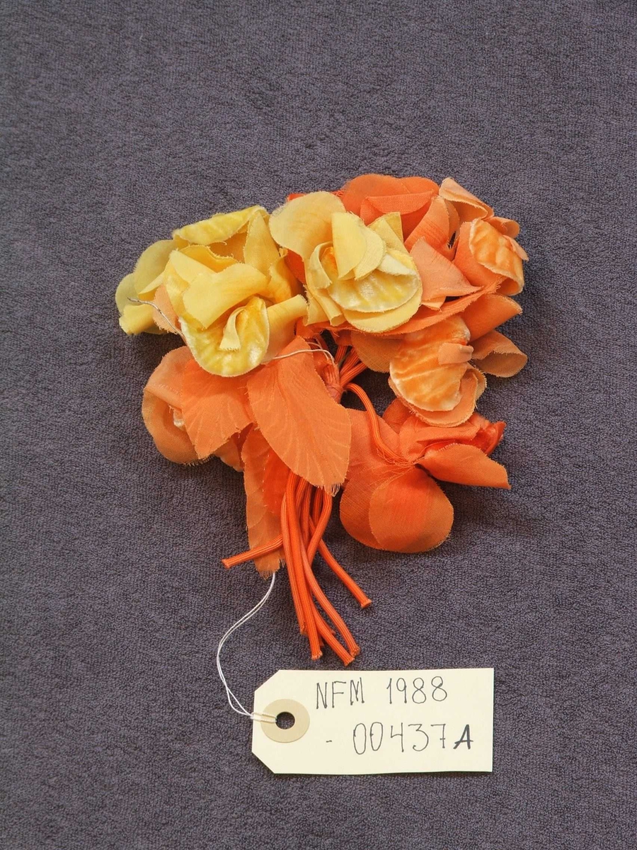 Seks ulike stoffblomar til pynt på drakt eller hatt. a: Bukett - orange/gul. b: Bukett - kvit/grøn. c: Rosett - svart/burgunder/rosa. d: Bukett - grøn/lilla. e: Bukett - grøn/lilla. f: grein - lys rosa. 