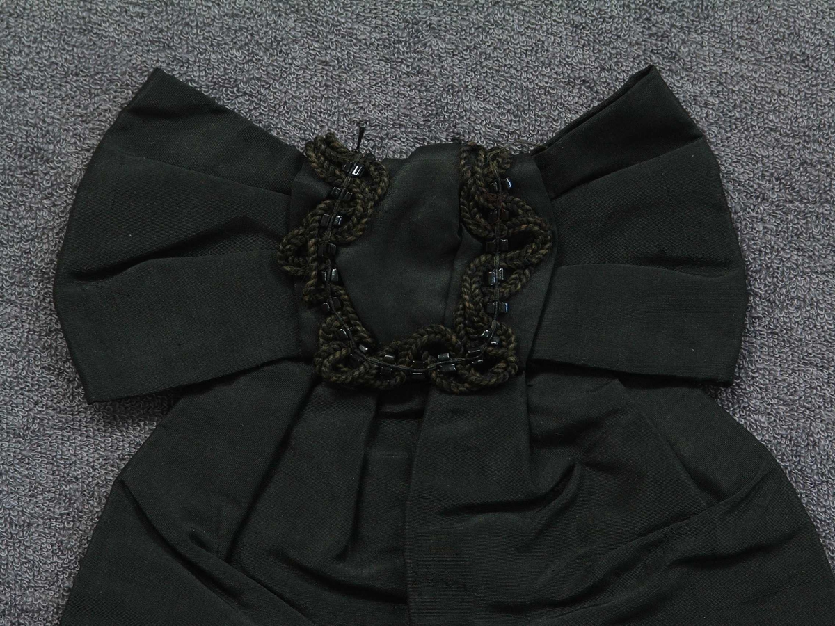 Svart sløyfe, pynt til bluse eller hovudplagg. Silkefrynser, fløyelsband, glasperler sydd på. Fôra.