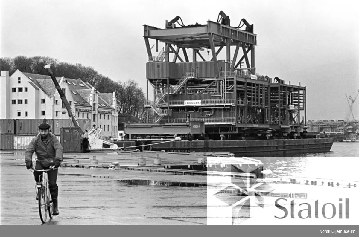 En modul som er klar for montering på dekket til Statfjord C, som under bygging ved Moss Rosenberg Verft i Stavanger, ligger klar på en lekter i Stavangers havnebasseng.
Verftsområdet skimtes i bakgrunnen.