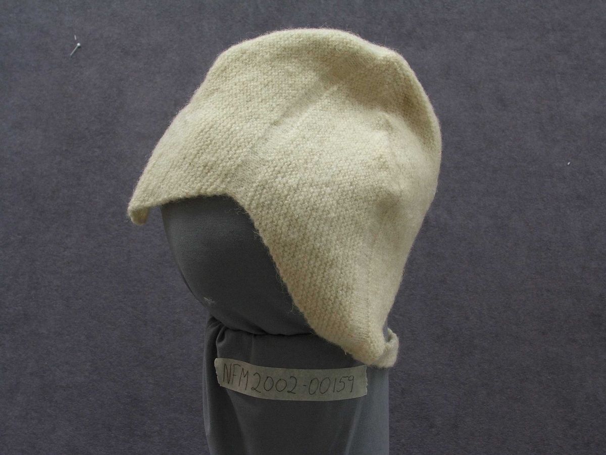 Strikka barnehue. Slags hjelm-fasong med ein spiss ned i panna. Strikka band til å ha under haka og knappe fast på andre sida.