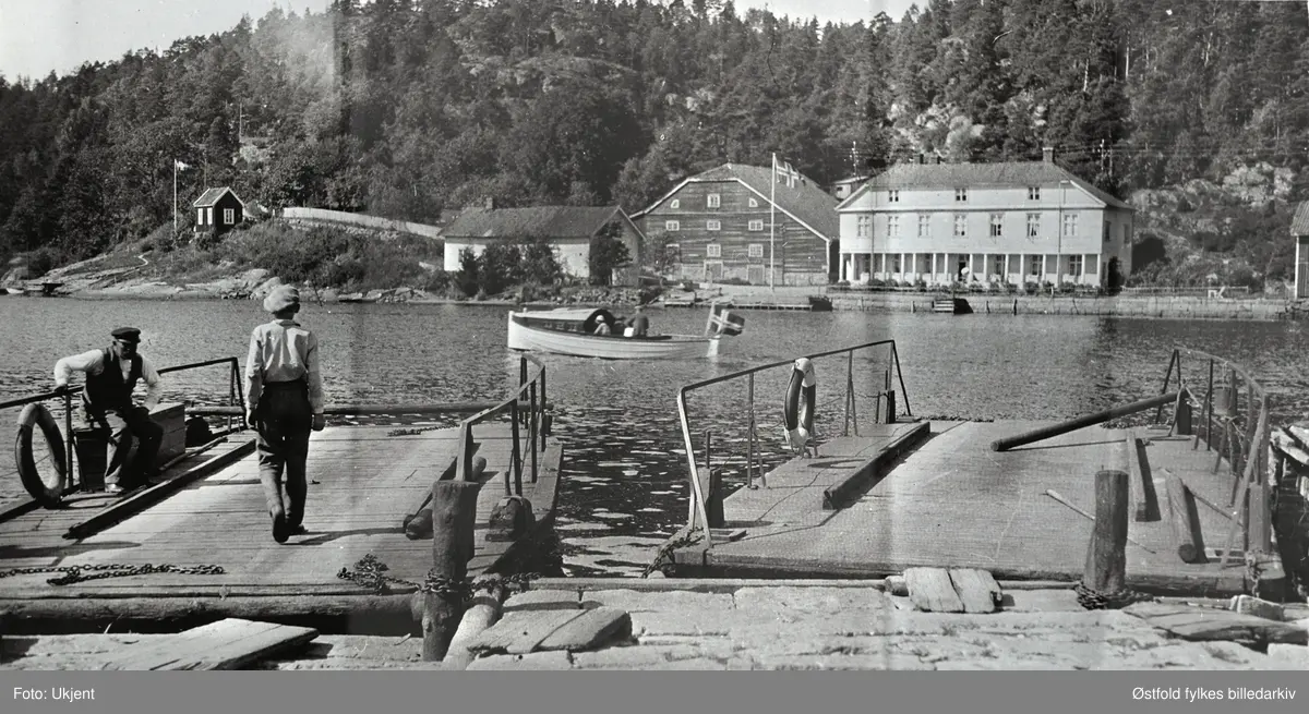 Svinesund fergested, Berg i Halden. Amatørfotografi tatt fra svenskesiden, ant. på 1930-tallet, mot Svinesund tollstasjon. Fergene/lekterne ble dratt over med en båt. Midtfjords en fritidsbåt. Til venstre for tollstasjonen uthus, og ei hytte helt ytterst til venstre.