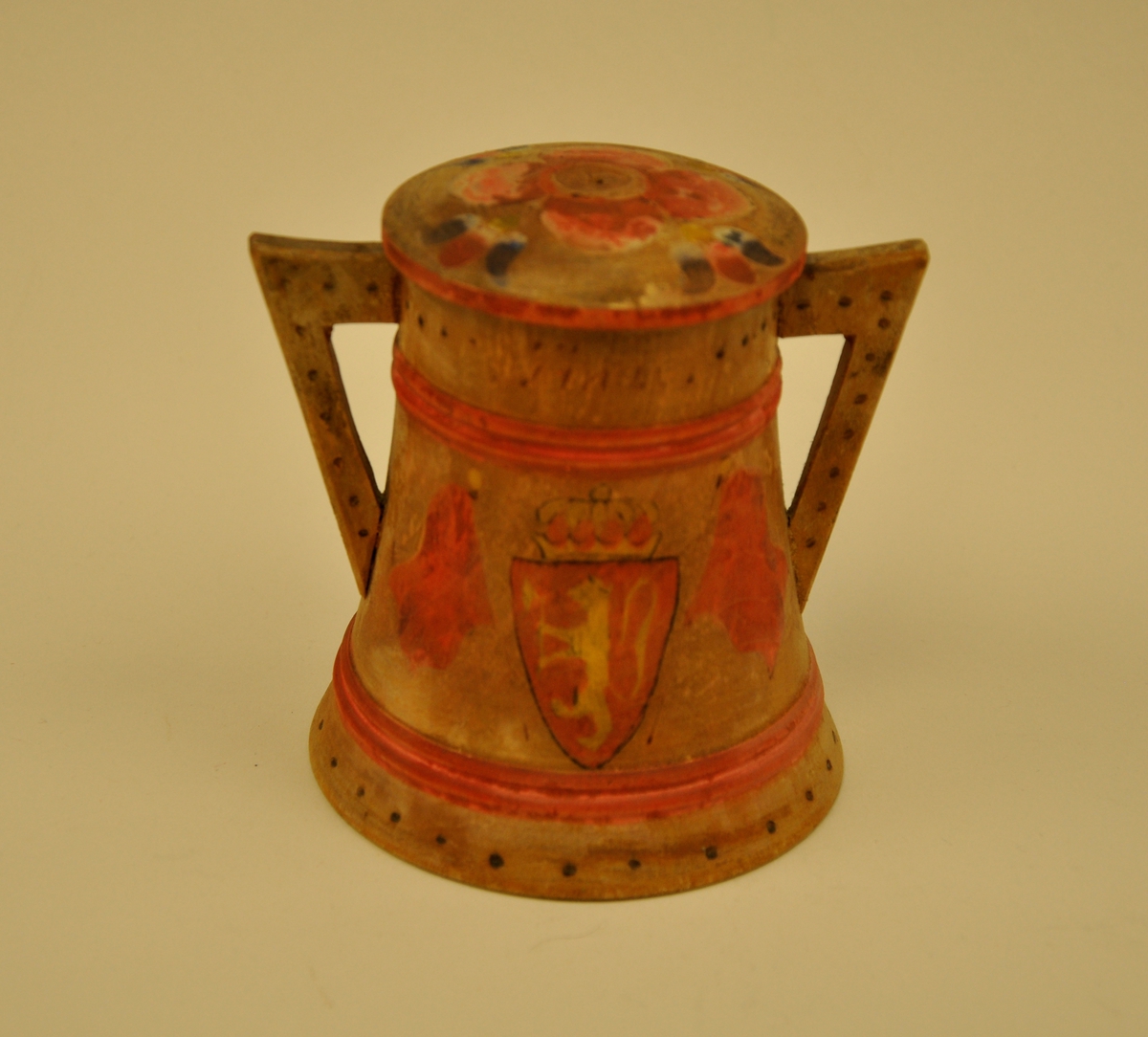 Begeret er breidast nede og smalnar jamt av oppover til kanten. Det har ei klar tredeling som kjem av stripene som skal forestille vidjeband. Dei tre felta har ulik dekor; det underste har ein ring rundt med svidde prikkar, det midterste har det norske våpenskjoldet på eine sida og ein slags rosemåling på den andre sida og det øverste har ein ring rundt med prikkar og innskrift. Hankene er nesten rettvinkla og dekorert med svidde prikkar. Loket er lett bua og har lik rosemålingsdekor med raud rose som midtpartiet