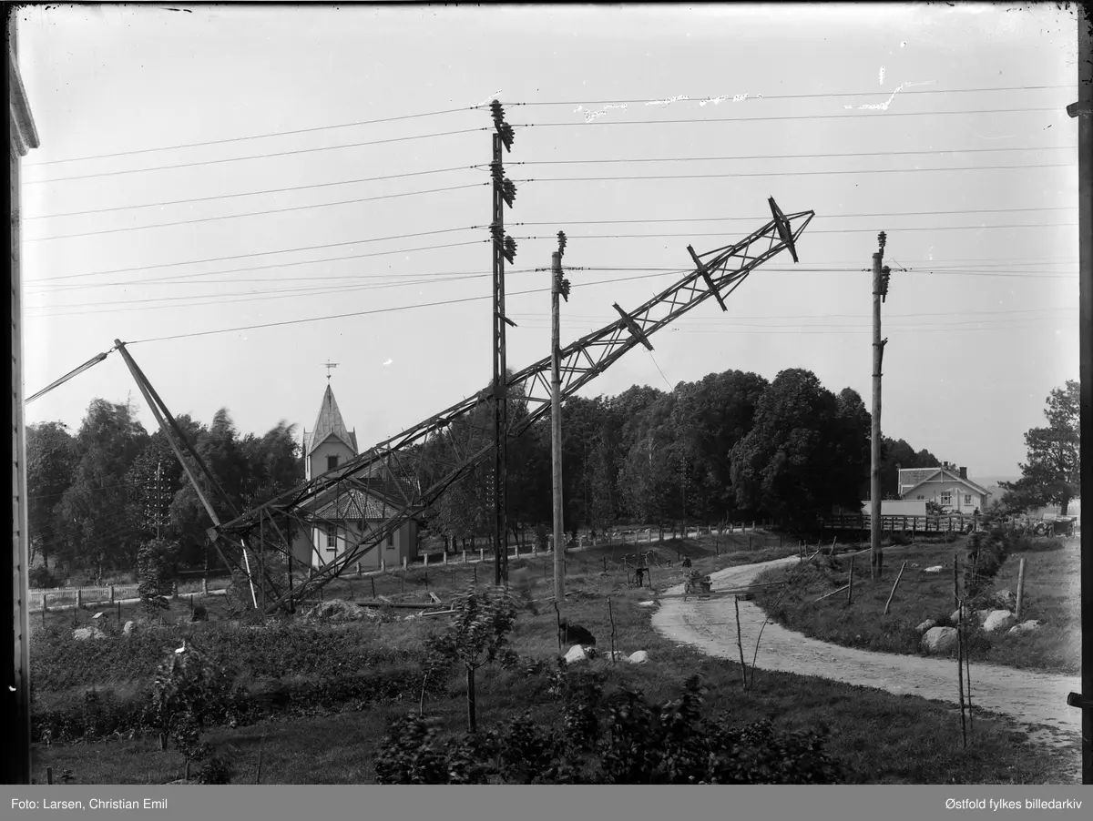 Hafslund, kraftstasjon, utendørs, heising, montering av transformatormast, Hafslund kirke og kapell i bakgrunnen.
Det lille huset er en kiosk for tipping og tobakk mmdrevet av Andersen. . Åpna på 1930-tallet. Fru Bergljot Karlsen (søster til Asbjørn Andersen)  sto i kiosken på 1950-60-tallet. Revet pga veibygging.
Tante Nikoline boddei det store huset (tante til informant).