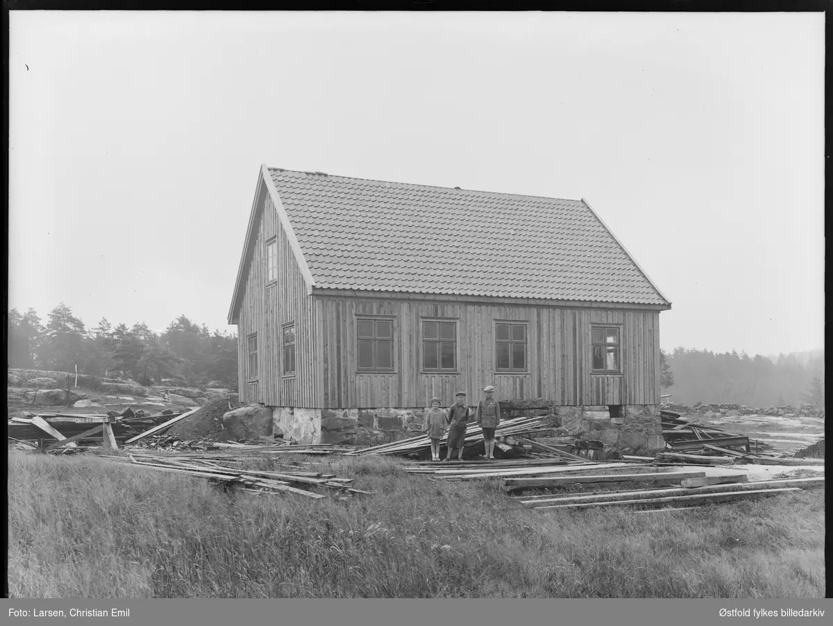 Gammelt trehus med tre barn utenfor. landlig plankerester rundt. Bygging av skole, eldre enn 1942 vel?
ukjent?