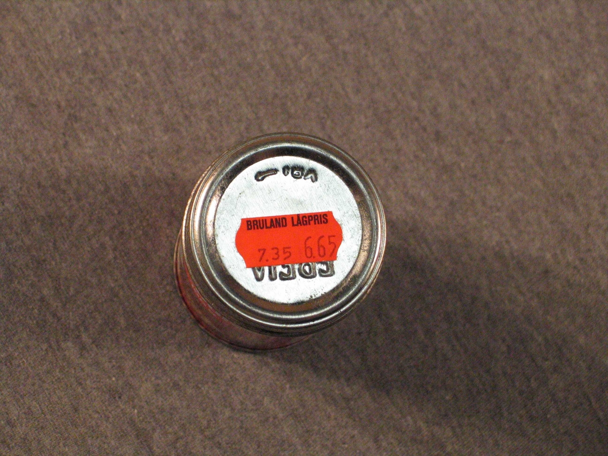 Rett blekkboks med skrulôk. Kring halvfull med bakepulver.
På lôket er orange prislapp frå Bruland Lågpris "7,35  6,65". Truleg betyr det  "vanleg pris" og "vår pris". det er strekkode på boksen, men butikken har truleg ikkje hatt avlesingsutstyr