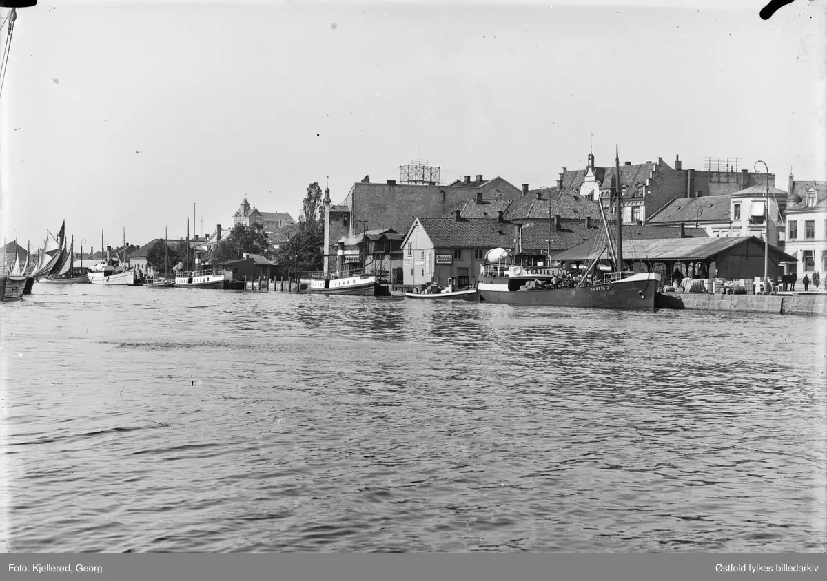 Dampskipsbrygga i Fredrikstad, med båten Trafik 3 ved kai, flere dampbåter ligger til venstre for den. i bakgrunnen forsamlingshuset Valhalla bygd 1870, avholdslosje. 

Dampskipsbrygga med et stort skur som må ha blitt brukt til å plassere varer som skulle lastes/losses fra dampbåtene som la til her. Fisketorvet lå helt til venstre i fotoet - der vi ser båter med seil.