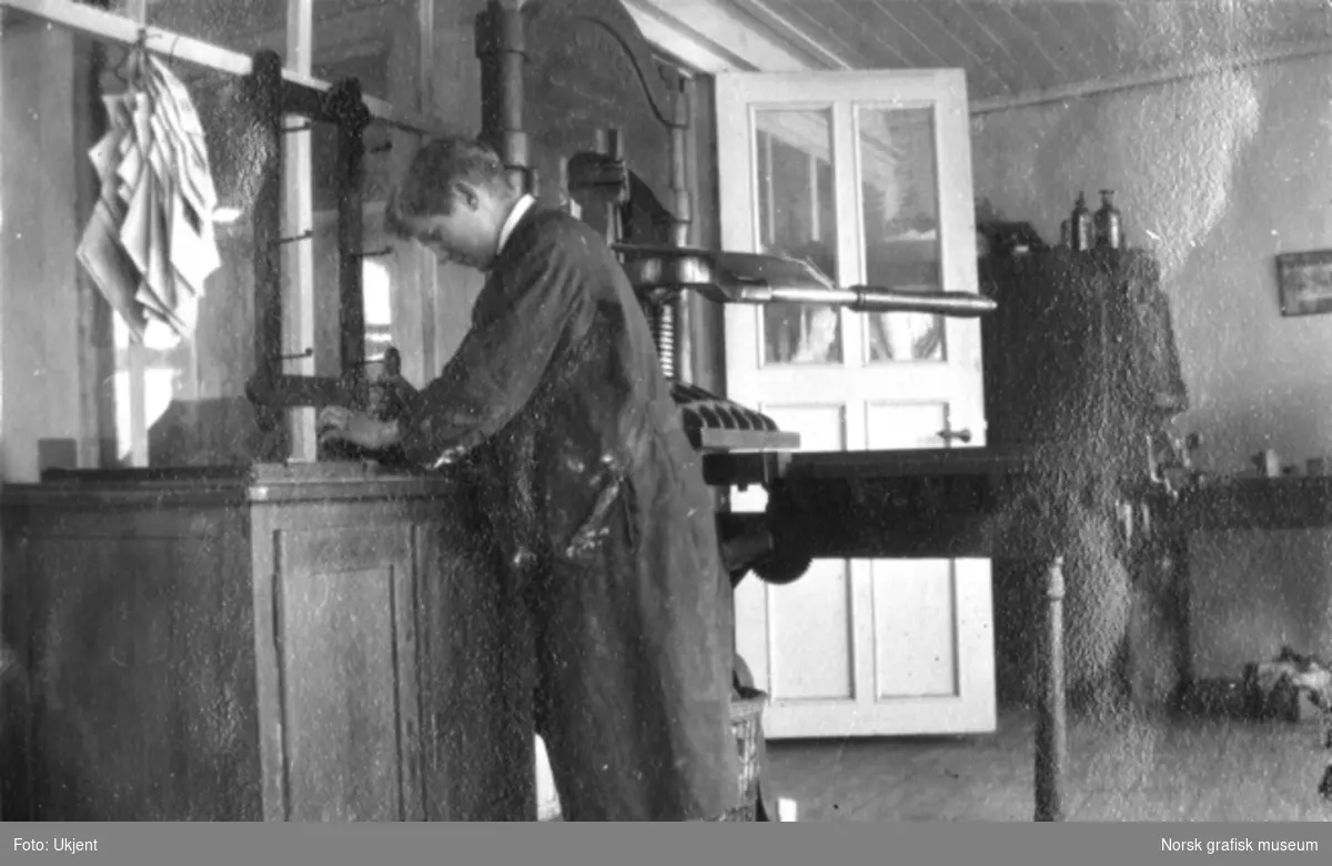 En ung mann i arbeidsfrakk står ved en arbeidsbenk.

Albumtekst:
Overtrykker Olaf Jakobsen
1919