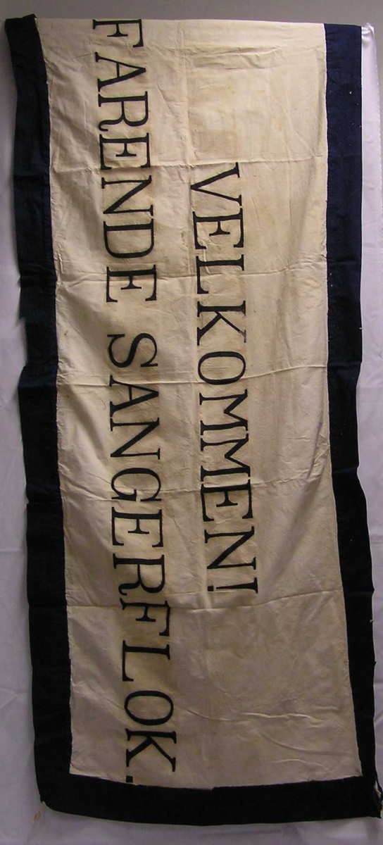 Bred stoffremse med bokstaver. Bokstaver er skrevet på stoffet.Kantet med kontrastfarge. Hastverksarbeid.