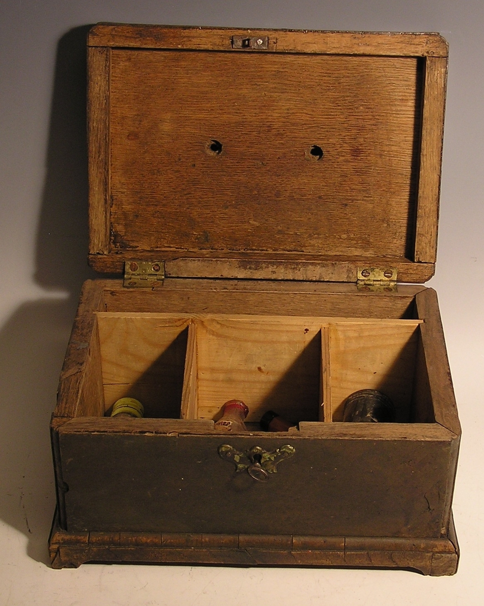 Rektangulær skrin med lokk og nøkkelhull. Liten nøkkel ligger i hullet.  Fotliste. Rommet er inndelt og inneholder små medisinflasker, krem og hodetabletter.
Ligner liten skipskiste.