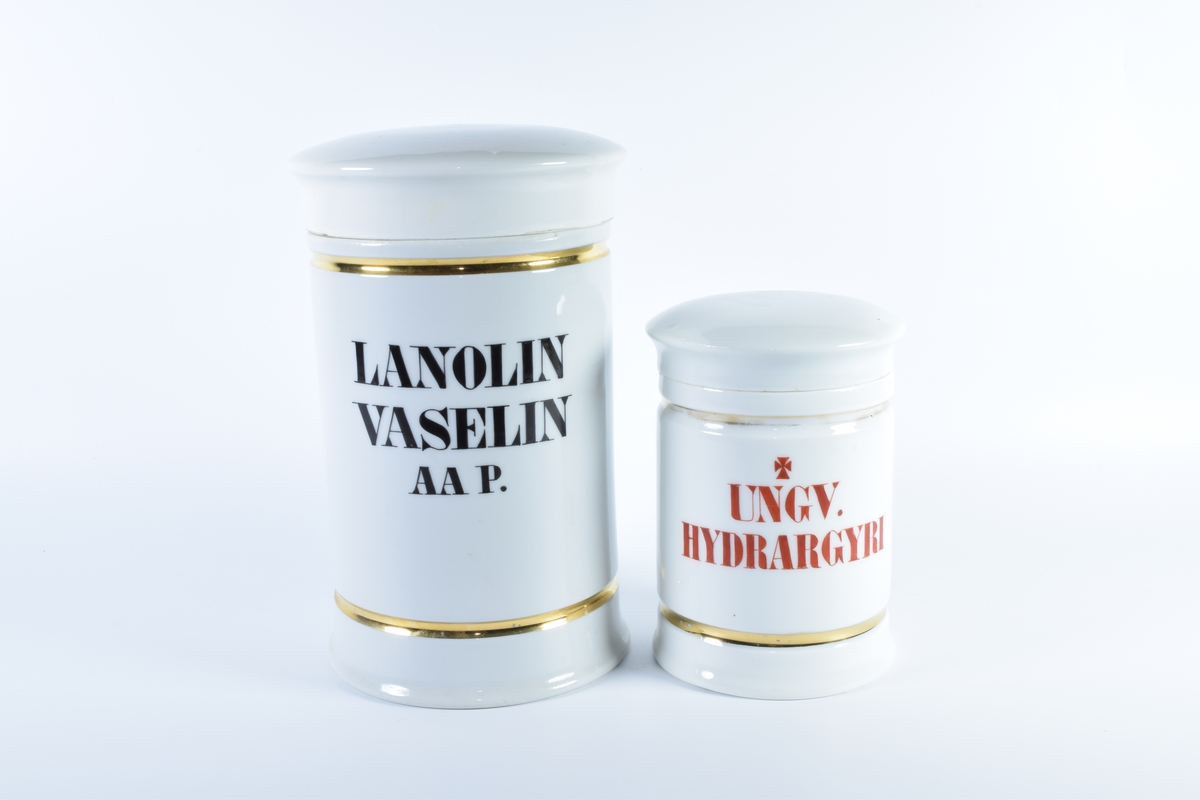 Seks sylindriske porselenskrukker med flatt lokk. Samtlige er dekorert med gullborder øverst og nederst og har skrift i svart eller rødt.