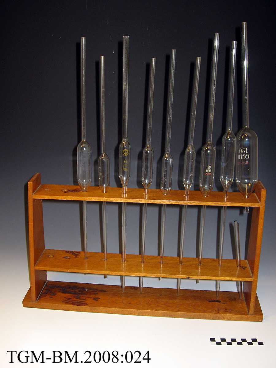 9 glassrør, med kul (kolbe) på midten og pipette-hull i den ene enden. Det er plass til 2 rør til i trestativet.