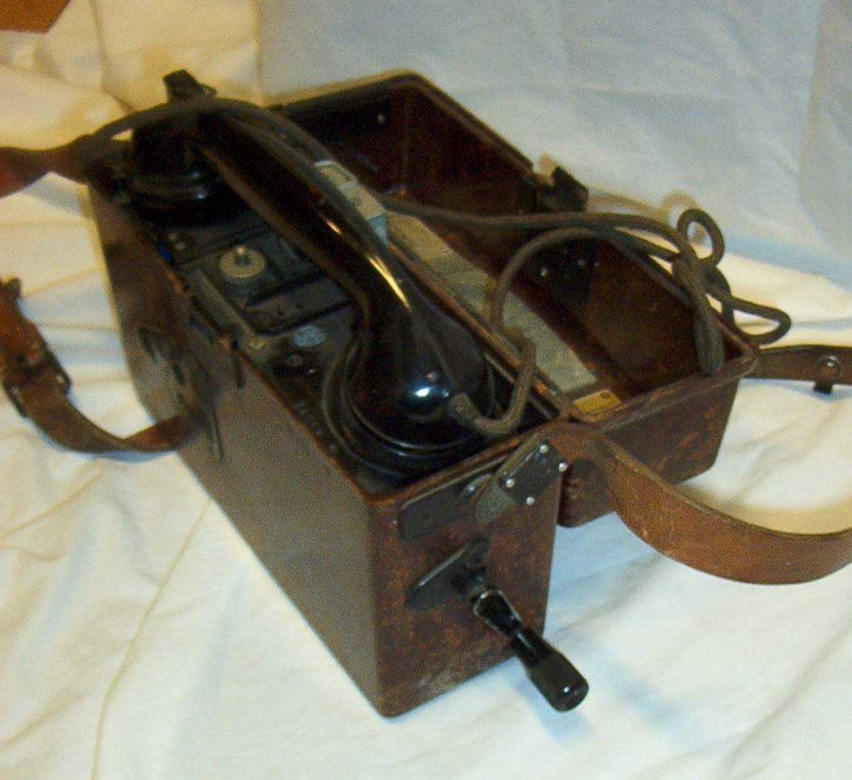 Felttelefon. Feldfernsprecher 33, FF33, tyskprodusert. Serienummer 74058.  Produksjonsår 1941. Telefonen er innebygd i bakelittkasse med bæresele. Hvit kodelapp montert på lokket. Det tyske alfabet står skrevet på lokket.