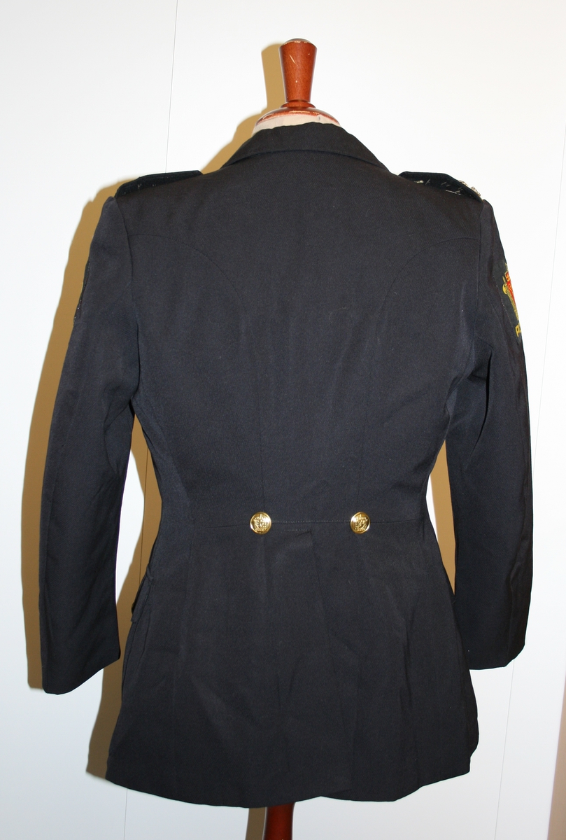 Foret, sort jakke med gullforgylte eikeløvsnåler på kraven. 4 gullforgylte knapper med riksvåpen i front og to ved splitten bak. Epåletter i flettet gull med fire stjerner og eikeløv (politidirektør). Fire lommer med klaff og knapp. Politimerke med riksvåpen på overarmene. Navneskilt i sort plast med gul skrift og riksvåpen. To ekstra navneskilt medfølger.

Knelangt, sort skjørt med glidlås bak.

Et kryssbandolær med gullforgylt rektangulær spenne dekorert med riksvåpen.

Et bredt lærbelte med gullforgylt rektangulær spenne dekorert med riksvåpen.

Et smalt lærbelte med gullforgylt rektangulær spenne dekorert med riksvåpen.

Politilue med hvit pull og luemerke i gull og rødt og eikeløvsbroderier i sort og gull. To forgylte knapper holder luesnoren på plass. (Lue for vinterhalvåret (med sort pull) registrert på NRM.03690)

Slips, skjorte og hvite hansker medfølger ikke.