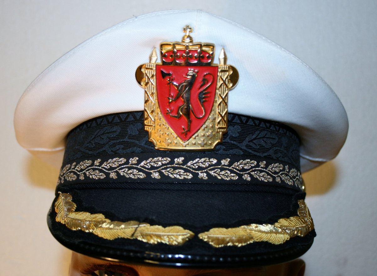 Foret, sort jakke med gullforgylte eikeløvsnåler på kraven. 4 gullforgylte knapper med riksvåpen i front og to ved splitten bak. Epåletter i flettet gull med fire stjerner og eikeløv (politidirektør). Fire lommer med klaff og knapp. Politimerke med riksvåpen på overarmene. Navneskilt i sort plast med gul skrift og riksvåpen. To ekstra navneskilt medfølger.

Knelangt, sort skjørt med glidlås bak.

Et kryssbandolær med gullforgylt rektangulær spenne dekorert med riksvåpen.

Et bredt lærbelte med gullforgylt rektangulær spenne dekorert med riksvåpen.

Et smalt lærbelte med gullforgylt rektangulær spenne dekorert med riksvåpen.

Politilue med hvit pull og luemerke i gull og rødt og eikeløvsbroderier i sort og gull. To forgylte knapper holder luesnoren på plass. (Lue for vinterhalvåret (med sort pull) registrert på NRM.03690)

Slips, skjorte og hvite hansker medfølger ikke.