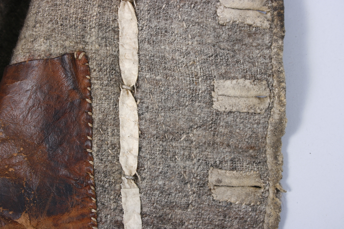 Dobbeltknept skinnvest med 9 knapper og passepoilerte knapphull på hvert framstykke. Knappene er festet med en skinnreim på innsiden . Den er sydd fast til foret. Øverste knapphull på høyre framstykke er sydd med knapphullsting. Knappene er siselerte med bokstaven B i midten med en bord rundt.  Den nederste knappen på begge framstykkene er mindre enn de andre og har ikke samme mønster som de andre. Vesten har 1 brystlomme og 2 lommer i livhøyde. 1 innerlomme i skinn er sydd fast til foret. Foret er sydd sammen av mange små stoffbiter i 2 farger. Foret og skinnet er stukket sammen. Bakovertrekte sidesømmer. Påsydd skinnkant rundt halsrigning og langs begge sider MF. Framstykkene går ned i en spiss MF.