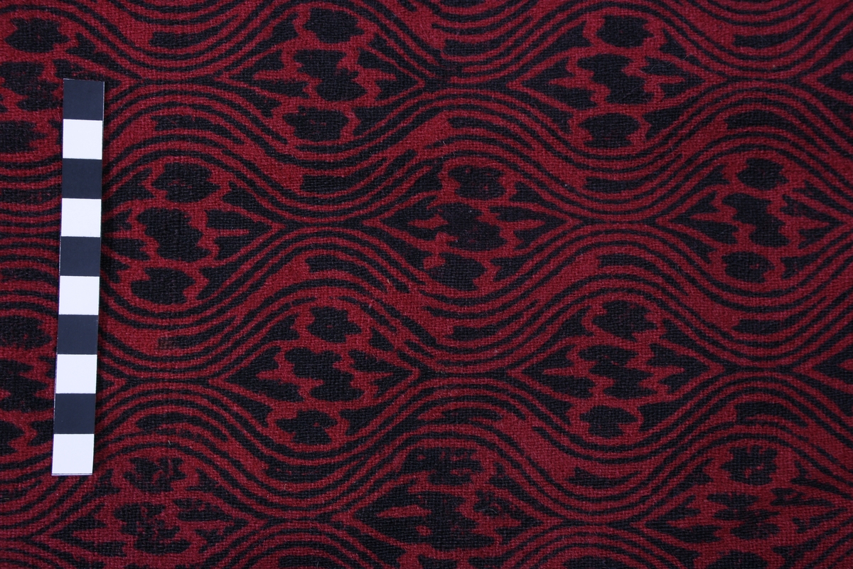 Ulveskinnspels, Lang og noe utskrådd. 
Sydd sammen av mange smale pelsstykker, to i høyden. En liten splitt midt bak. Ermer sydd sammen av mindre pelsstykker. Ermene har en liten oppbrettet fald av pelsen i nedkant, på resten av plagget er pels og fór sydd sammen kant i kant, ute belegg eller oppbrettet fald. Sjalskrage med underkrage av sort kunstpels. Underkragen har søm midt bak. 
Fóret med rødt klede med sort trykk, også i ermene.
Hele plagget er håndsydd med grov tråd, selve pelsen med ubleket lintråd. Fóret er sydd sammen, og sydd til pelsen, med ubleket eller sort bomullstråd. Fóret har sidesømmer, men ingen søm i ryggen. Ryggstykket er kvadratisk med trådrette sider. Forstykkene er trådrette midt foran og skrådd i siden. I sidene er det satt inn en liten kile nederst. 
I nedkant av kragen i venstre side er det en stor sølvhekte, gravert med blomstermotiv. Ingen tegn til annen lukning.  
Stor lærhempe i nakken.