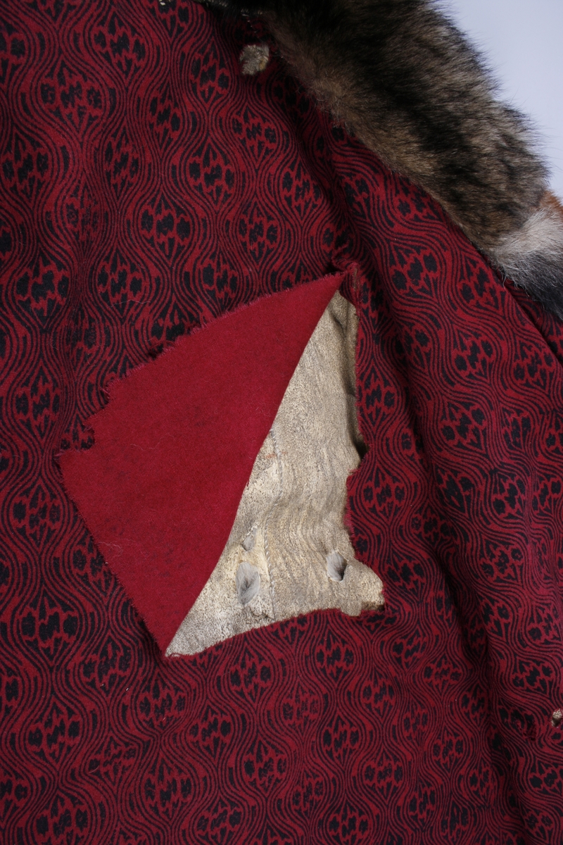 Ulveskinnspels, Lang og noe utskrådd. 
Sydd sammen av mange smale pelsstykker, to i høyden. En liten splitt midt bak. Ermer sydd sammen av mindre pelsstykker. Ermene har en liten oppbrettet fald av pelsen i nedkant, på resten av plagget er pels og fór sydd sammen kant i kant, ute belegg eller oppbrettet fald. Sjalskrage med underkrage av sort kunstpels. Underkragen har søm midt bak. 
Fóret med rødt klede med sort trykk, også i ermene.
Hele plagget er håndsydd med grov tråd, selve pelsen med ubleket lintråd. Fóret er sydd sammen, og sydd til pelsen, med ubleket eller sort bomullstråd. Fóret har sidesømmer, men ingen søm i ryggen. Ryggstykket er kvadratisk med trådrette sider. Forstykkene er trådrette midt foran og skrådd i siden. I sidene er det satt inn en liten kile nederst. 
I nedkant av kragen i venstre side er det en stor sølvhekte, gravert med blomstermotiv. Ingen tegn til annen lukning.  
Stor lærhempe i nakken.