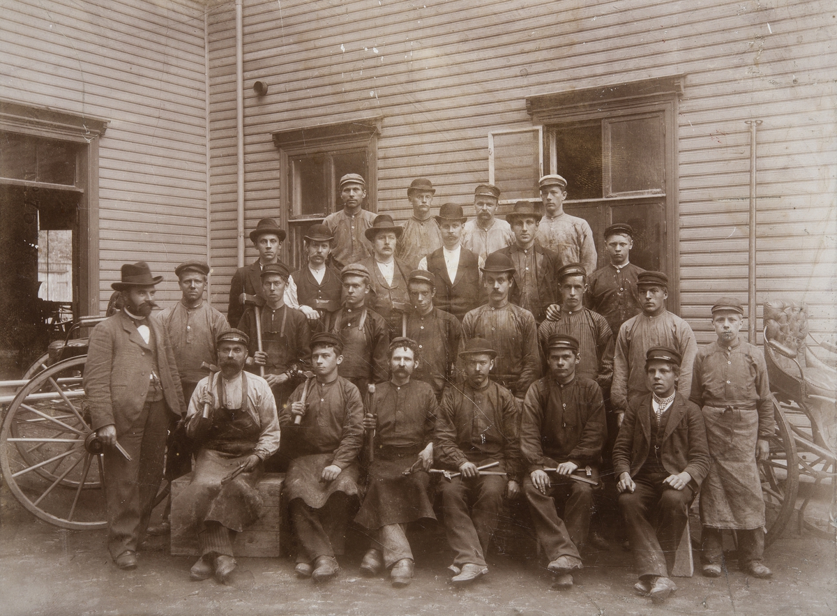 Hamar, Torggata 11, gruppe 25 arbeidere ved P. Norsengs Vognfabrikk. Mannen med sort hatt til venstre er innhaver av fabrikken Peder Norseng, smed og snekker,