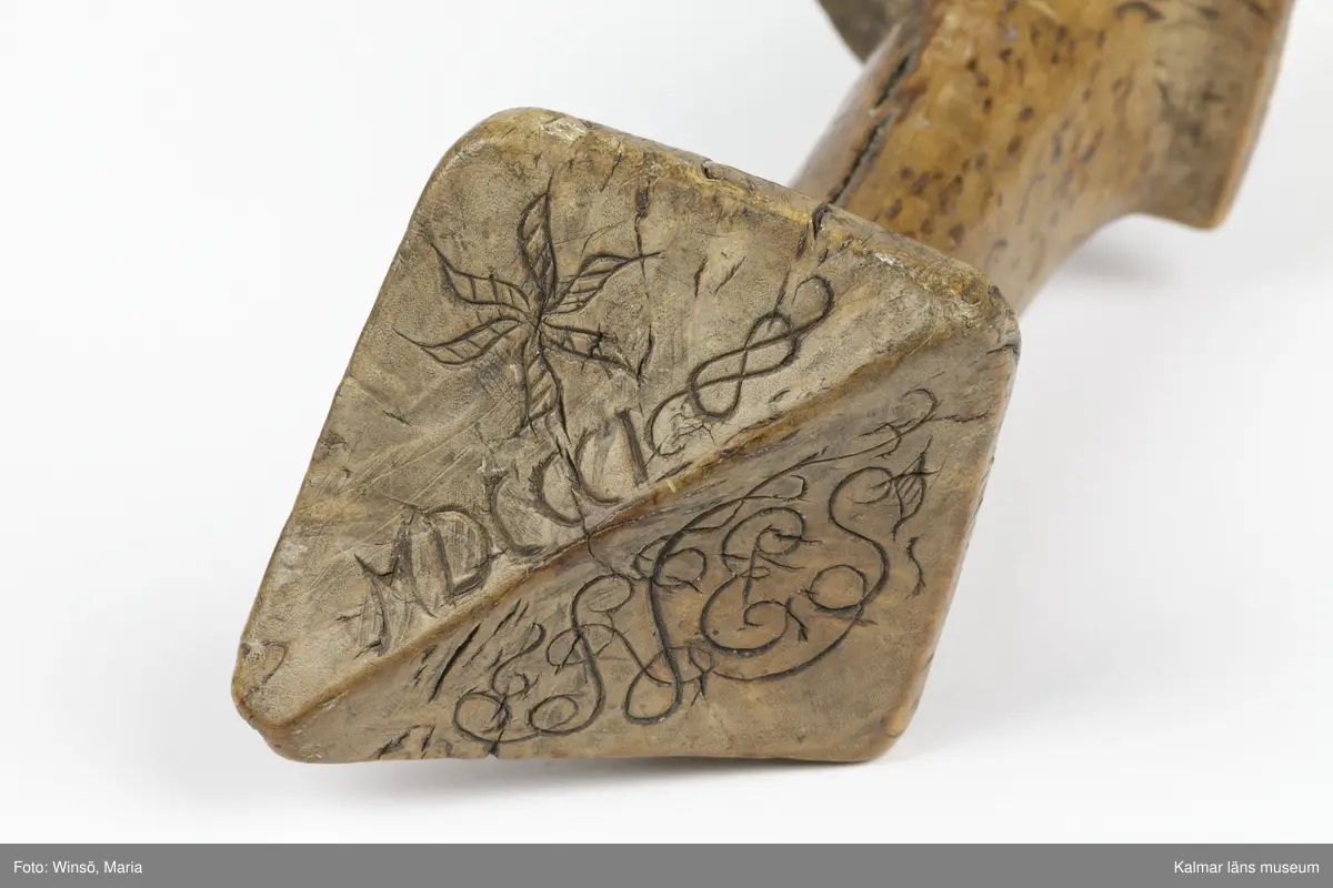 KLM 3120. Skära, vinkelskära, trä, metall. Vinkelskära med bågböjt blad av järn, fastnitat på skaftets ena sida. Skaft av masurbjörk med fyrsidig knopp med skarp mittrygg. På knoppens översida inskuret årtalet MDCCCI (1801 och blommor och rankor). På handtaget nära bladet inbränt PNS. Bladet märkt A. Användes för att skära av säden.