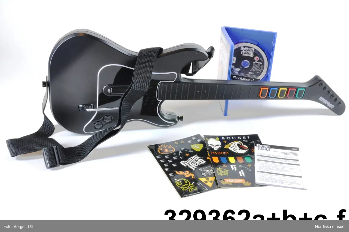 TV-spelet "Guitar Hero III Legends of Rock" med förpackning. 
a+) Elgitarr med avtagbar hals, av svart plast, svart axelrem av syntettextil med konstläder (plast) och plastöglor.
b+) 2 ark med klisterbilder att fästa på gitarren
c) Broschyr med instruktioner om funktion och säkerhet på flera olika språk.
d) Fodral av blå plast med inplastat omslag av papper med text. På framsidan "Playstation 2 / Guitarr Hero III LEGENDS of ROCK" och bild på hårdrockare. Baksidan bl.a. "SLÄPP LOSS DIN INRE ROCKLEGEND / Över 70 rockiga låtar.".
e) CD-skiva med programvara (förvarad i fodral d).
f) Instruktionsbok på de nordiska spårken (förvarad i fodral d) 
g+) Förpackning av papp. Ytterfodral med text och bilder. Inre lådan med inredning för de olika delarna.
 
Tv-spelet är avsett för spelplattformen Playstation 2, vilket är en vanlig spelplattform. Spelet går ut på att det spelas upp en låt (man väljer själv låt och nivå) och ska sedan försöka spela på gitarren genom att trycka på knapparna och på så vis lyckas spela samma ton som musiken spelar samtidigt.

Vid förvärvet avlägsnades plastpåsar som del av a och b låg i, samt två 1.5volts-batterier av märket Duracell som låg i gitarren, då de ej bedömdes möjliga att spara. Även fyra papperspåsar med Silicagel (för att hindra att fukt skadar elektronik mm) togs bort.

Nyinköp den 2008-02-20 för att rekonstruera julkklappsönskemål julen 2007 från Erik Thomelius född 1999, Vaxholm. Inköpt av Nordiska museet för 439 kr. Ingår i projektet "Barn tar plats". Se dokumentation i arkivet D455.
/Ulf Hamilton 2008-05-27     