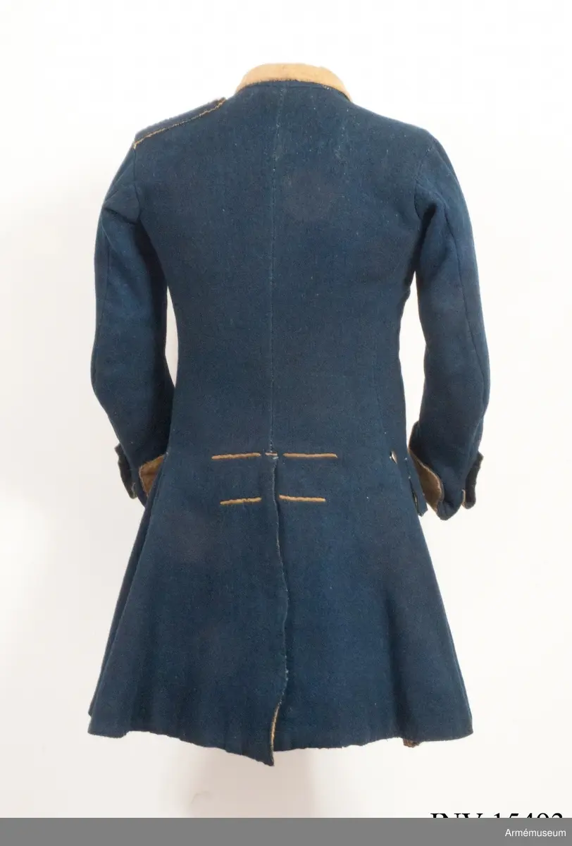 Rock av blått kläde med gul krage och ärmuppslag. Fodrad med gul boj i livet och med linne i ärmarna. Försedd med tennknappar.