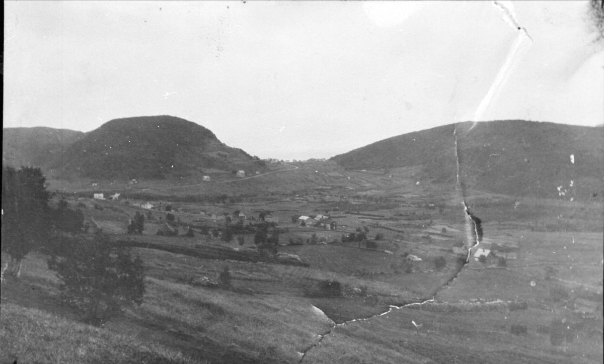 Landskap, bebyggelse og hesjer fotografert fra Kilhusåsen, ovenfor Høgfors (?), mot Sama- og Harstadåsene i bakgrunnen.