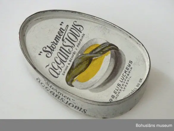 Närmast oval burk, dekor tryckt direkt på plåten i vitt och svart samt bild av ansjovis och äggskiva Text:" "Stormen" Äggansjovis skinn & benfri AB Elis Luckeys konservfabrik Samma bild och och text på baksidan.
Om givaren se UM026667