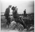 'Akka-expeditionen sommaren 1931: ::  :: Vy med 3 st män med havet i bakgrunden. Leonard Axel Jägerskiöld sitter på ett stenblock och kikar upp mot skyn, med kikare. Bredvid står Harald Alander. ::  :: Ingår i serie med fotonr. 2182-2234.'