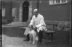 Paul Henrici sittande på träbänk med hunden Tyra, på Natushistoriska museet innergård.