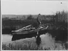 'Bilder från Hornborgasjön från: R. Söderberg: '' Hornborgasjön och dess fornsjöområde'' Del I 1932. ::  :: en man ståedens i en roddbåt  i en muddrignsränna efter Hornborgasjöns sista sänkning. Sjösänkning. ::  :: Ingår i serie med fotonr. 4245:1-35.'