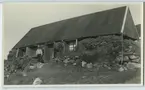 'Gamla snickaraffären och fängelset. En inuit(eskimå)man står intill dörren till huset. En grupp av 6 inuiter (eskimåer) sitter på en trätrappa till huset. Barn, kvinna, man. Kläder. Klädsel. ::  :: Enligt kuvertet som negativet låg i ''Trip to W-Greenland''. ::  ::  :: Ingår i serie Fotonr. 5217:1-103. Se även hela fotonr. 5202-5218 med bilder från Frits Johansen.'