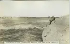 '''Tracking up the limestone rapids. The Pas. Man, Canada''.  2 män stående på bergshäll intill floden. ::  :: Ingår i serie Fotonr. 5218:1-12. Se även hela fotonr. 5202-5218 med bilder från Frits Johansen.'