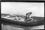 'Diverse fotografier från bl.a. dåvarande Nordrhodesia, nu Zambia, tagna av Konsul Magnus Leijer. ::  :: Ett barn sittandes i en eka, uppdragen delvis på strand. I båten ligger åror och 2 fåglar.'