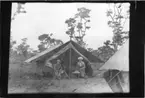 'Diverse fotografier från bl.a. dåvarande Nordrhodesia, nu Zambia, tagna av Konsul Magnus Leijer. ::  :: En kvinna och en man med en hund, båda sittande i öppningen av ett tält, i förgrunden är del av ytterligare ett tält synligt. I bakgrunden träd.'