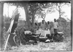 'Diverse fotografier från bl.a. dåvarande Nordrhodesia, nu Zambia, tagna av Konsul Magnus Leijer. ::  :: 4 st män/pojkar stående på rad bakom ett dukat bord, framför ligger 1 st man med pipa i munnen, i en solstol, även resväska, gevär och död fågel är synlig.'